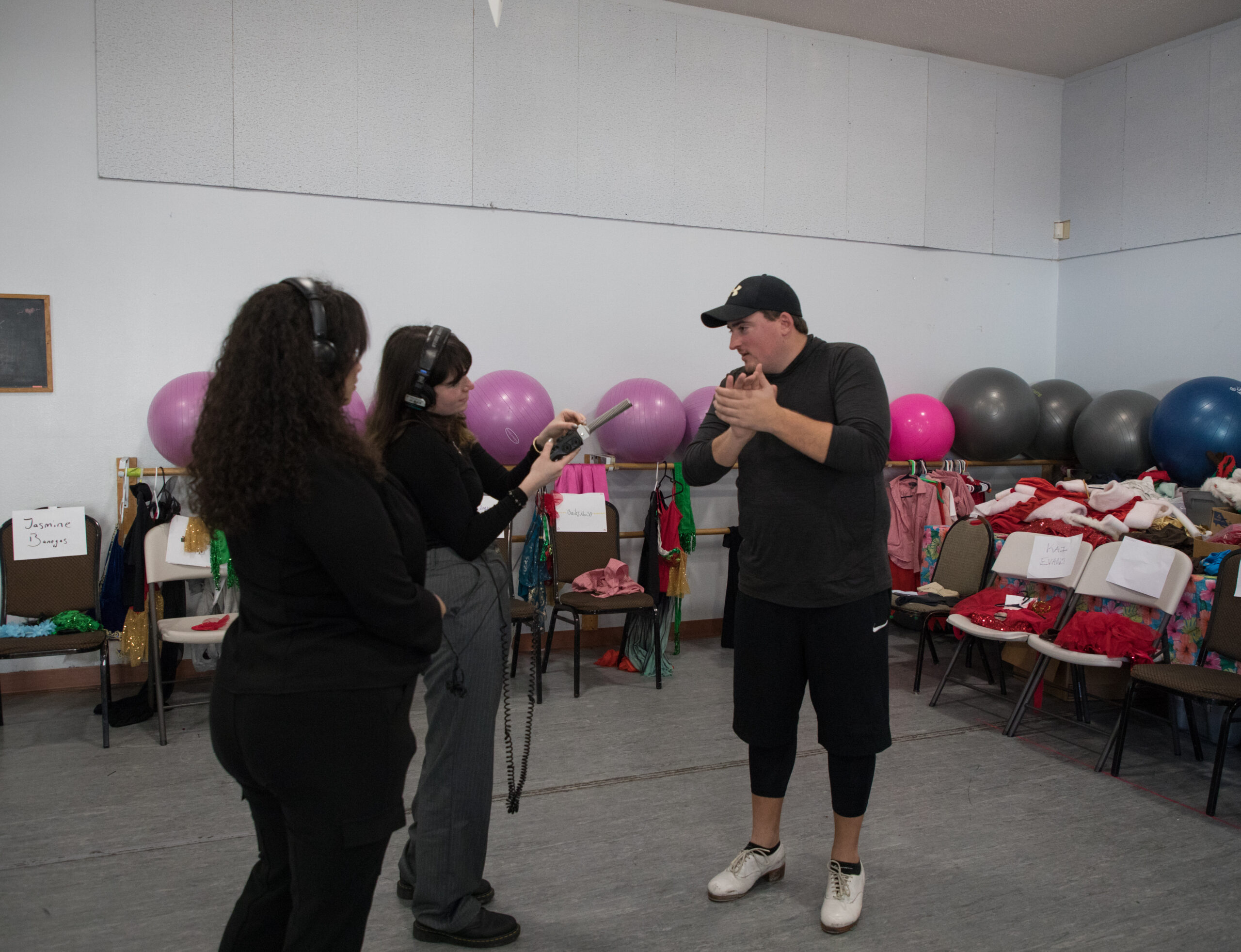 Two reporters record a dance coach with a microphone in a dance studio.