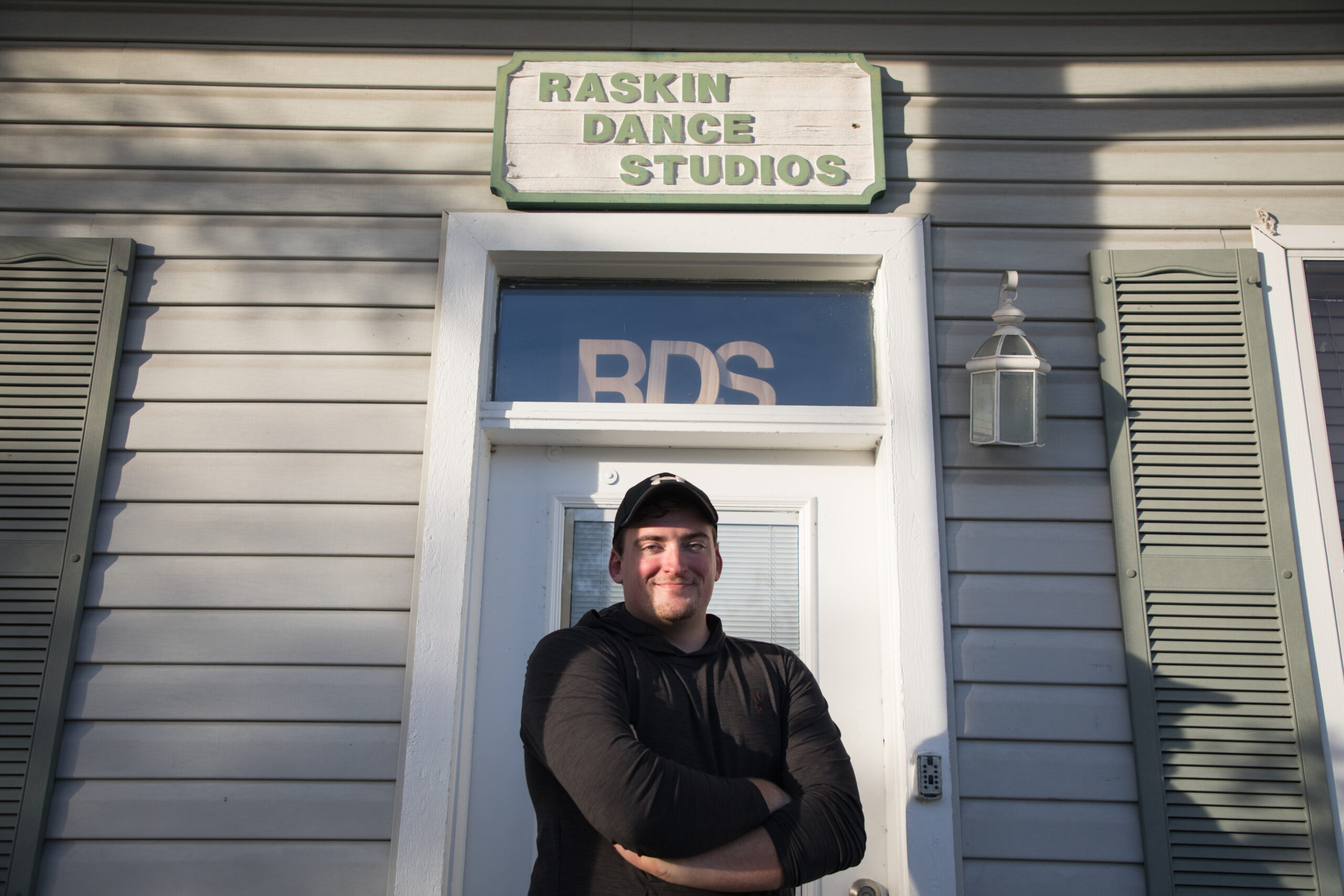 Josh Nixon poses in front of the Raskin Dance Studio’s front door. He crosses his arms and stands beneath the studio’s sign.