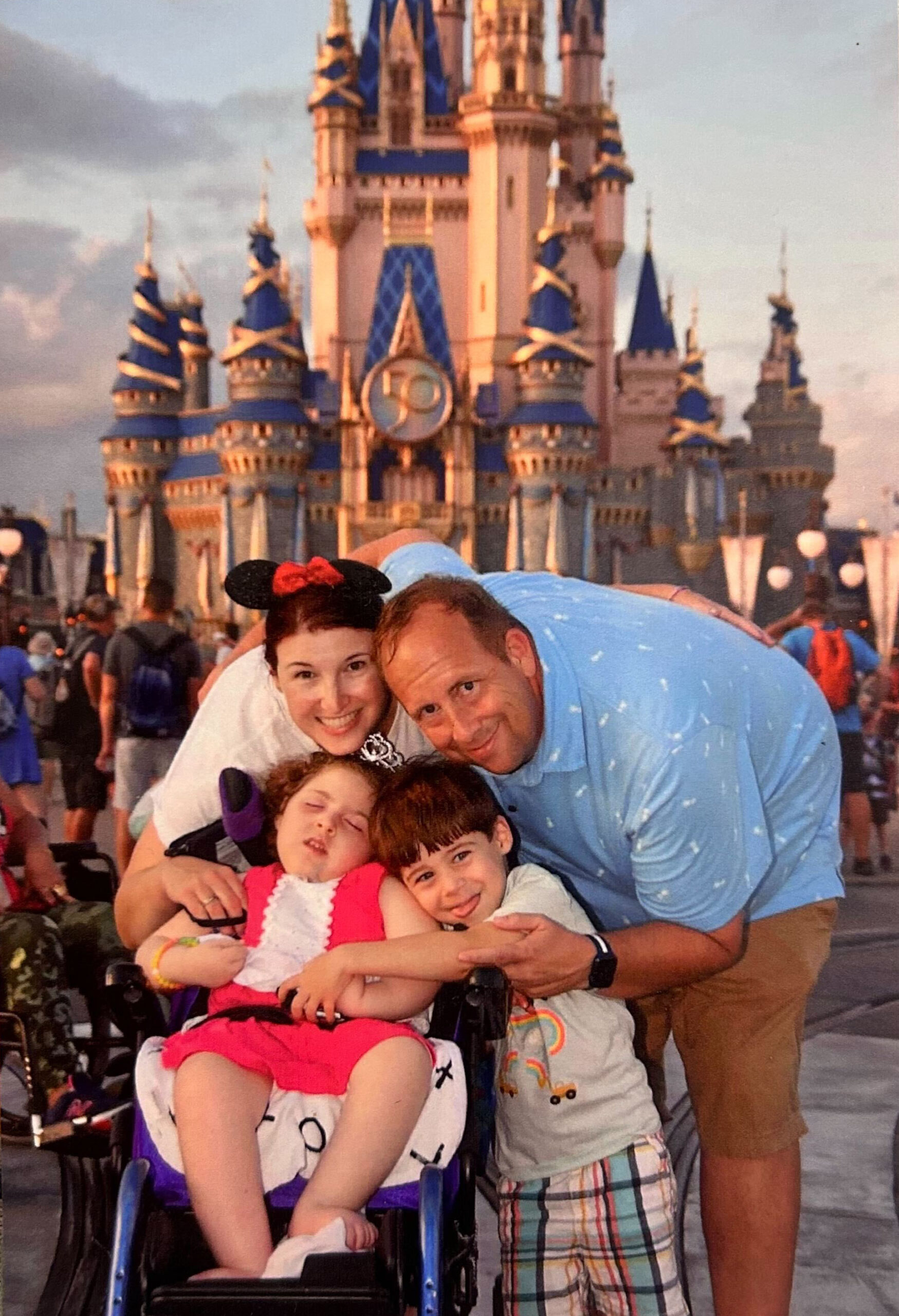 A husband, wife, and their son and daughter pose together for a picture in front of Cinderella Castle at Disney World. The daughter is dressed as a princess.